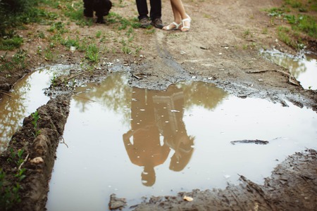 male and female feet are standing next to a puddle and reflected in itの写真素材