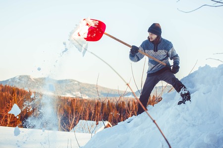 Happy young woman shovelling snow against blue skyの写真素材
