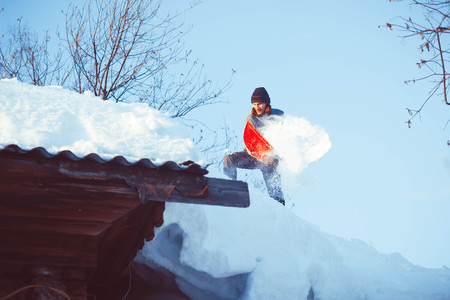 Happy young woman shovelling snow against blue skyの写真素材