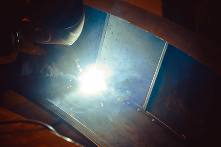 worker welding metal with sparks and smoke in the helmet