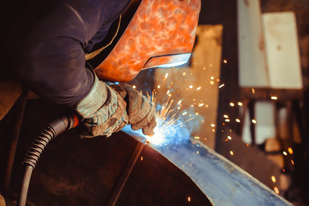 worker welding metal with sparks and smoke in the helmet