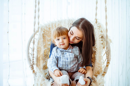 mother and son swinging on the swing at home by the windowの写真素材
