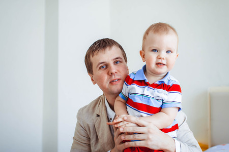 Happy father plays with his son sitting on the bed at home. Young man playing with little boy.の写真素材