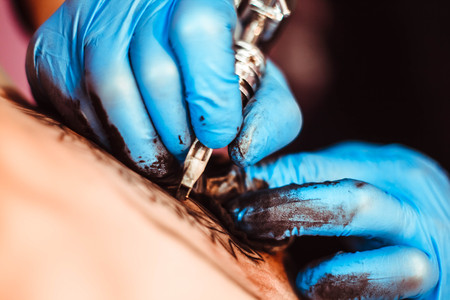 A professional tattoo artist makes a drawing on the machine. Tattoo on the body.の写真素材