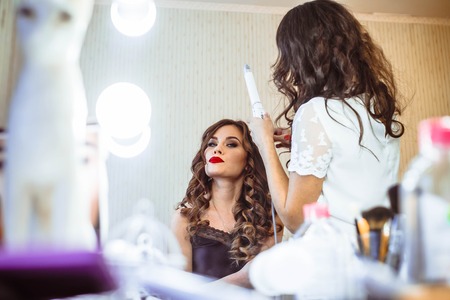 Hair stylist making ringlets to brunette woman. Hairdresser working with beautiful woman hair in hairdressing salon.の写真素材