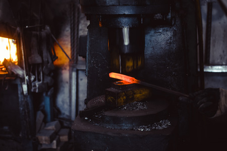 The blacksmith manually forging the molten metal on the anvil in smithy with spark fireworks