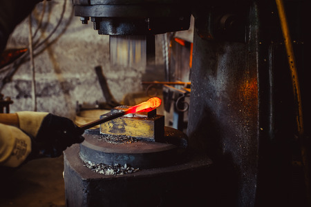 The blacksmith manually forging the molten metal on the anvil in smithy with spark fireworksの写真素材