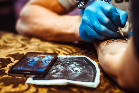 Russia, Novokuzneck, 5.07.2017: The tattoo artist makes a tattoo on the client's neck in the tattoo salon. The master does a tattoo in the studio. Close-up. Hard. Pain.のeditorial素材