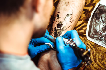 Russia, Novokuzneck, 5.07.2017: The tattoo artist makes a tattoo on the client's neck in the tattoo salon. The master does a tattoo in the studio. Close-up. Hard. Pain.のeditorial素材