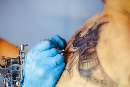 Russia, Novokuzneck, 5.07.2017: The tattoo artist makes a tattoo on the client's neck in the tattoo salon. The master does a tattoo in the studio. Close-up. Hard. Pain.のeditorial素材