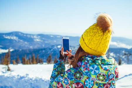 Russia, Siberiya, 8.03.2017: Senior woman with backpack holding camera and taking picture in winter mountains - rear viewのeditorial素材