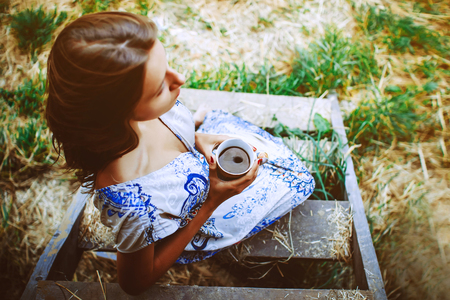 The beginning of autumn, happy girl near his country house, girl with white cup on the veranda of the house. girl drinking tea, woman with a cup of coffee.の写真素材