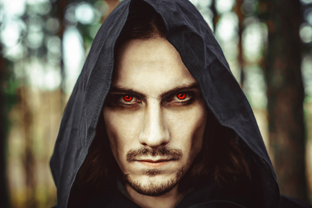 the vampire in the hood with glowing eyes in the forest