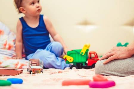 Happy funny little blond child playing with lots of toy cars indoor. Kid boy wearing colorful shirt and having fun at nursery.の写真素材