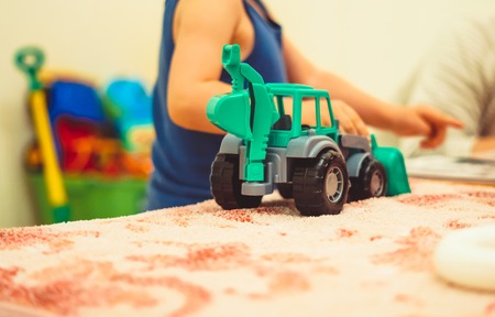 Happy funny little blond child playing with lots of toy cars indoor. Kid boy wearing colorful shirt and having fun at nursery.の写真素材
