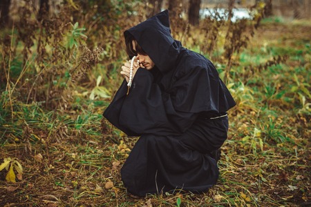 a monk in a black robe praying in the woods on his kneesの写真素材