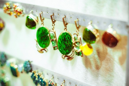 little gold earrings with precious stones and a white pearl in the middle on the counter of a...