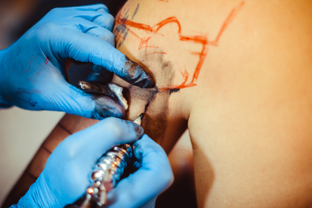 The tattoo artist makes a tattoo on the client's neck in the tattoo salon. The master does a tattoo in the studio. Close-up. Hard. Pain.の写真素材
