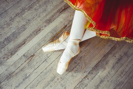 Beautiful legs of young ballerina who puts on pointe shoes at white wooden floor background, top view from above with copy space. Ballet practice. Beautiful slim graceful feet of ballet dancer.の写真素材