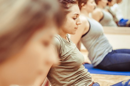 Beautiful girl in sportswear is doing yoga on yoga mat in sports hallの写真素材