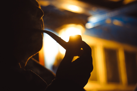 man Smoking pipe at night in the light of a lanternの写真素材