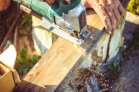 Man with protection gloves using an electric saw to cut a plank