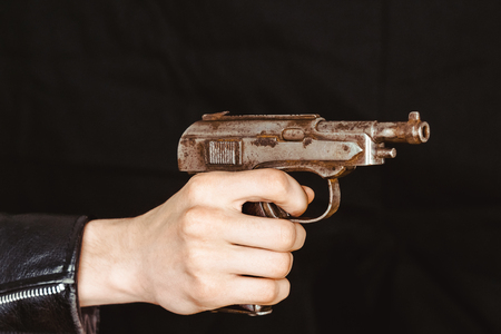 hand holding gun on black background in leather jacket