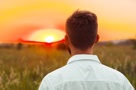 a man in a white shirt stands and looks at the sunsetの写真素材