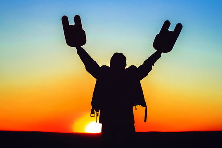 Hands with horns are raised up in a position standing at sunset in a leather jacketの写真素材