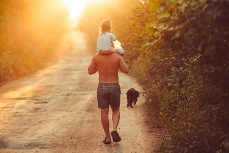 Father and his daughter playing outdoors. the child sits at the daddy on the neck, having lifted hands. against the sky in the sun. Happy loving family. Father's Dayの写真素材