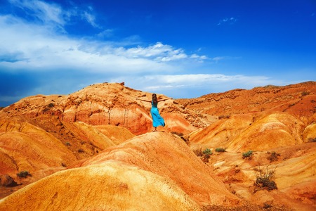 a young girl in a dress stands among the red mountainsの写真素材