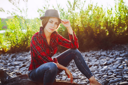young beautiful girl in a hat and shirt in the sun at sunsetの写真素材