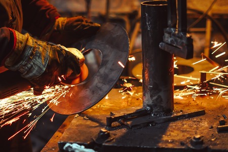 Craftsman sawing metal sparkles all around workshop. Working at noon.