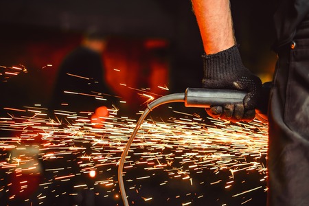 Craftsman sawing metal sparkles all around workshop. Working at noon.