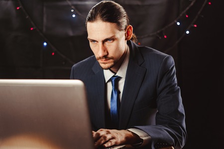 Businessman working on New Year's Eve. He was very tired and fell asleep behind his laptop. He wears a Christmas hat.の写真素材