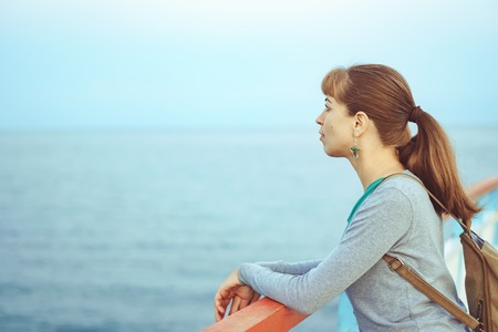 a beautiful girl is standing on the pier in a shirt and jeans in the eveningの写真素材