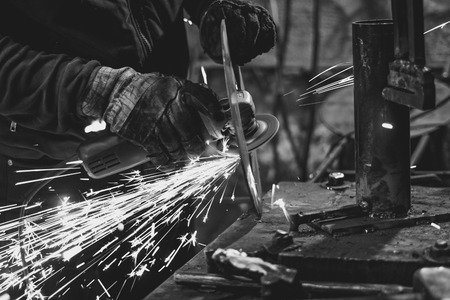 Craftsman sawing metal sparkles all around workshop. Working at noon.
