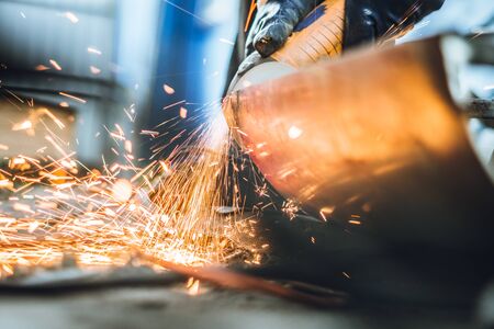 Craftsman sawing metal sparkles all around workshop. Working at noon.