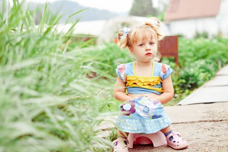 portrait of cute Happy little girl sitting on potty outdoorsの写真素材