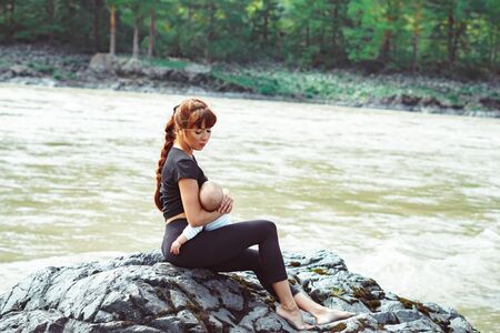 mother breastfeeding baby in nature in a picturesque place near the mountainsの写真素材