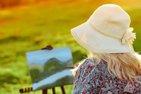 an elderly woman paints a picture in nature oil painting by the riverの写真素材