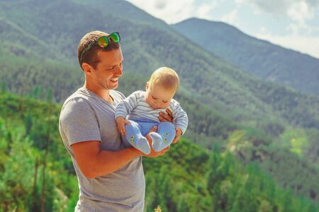 dad holding a baby in his arms against the mountainsの写真素材