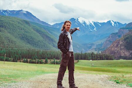the guy stands against the background of snowy mountains with snow-capped peaks