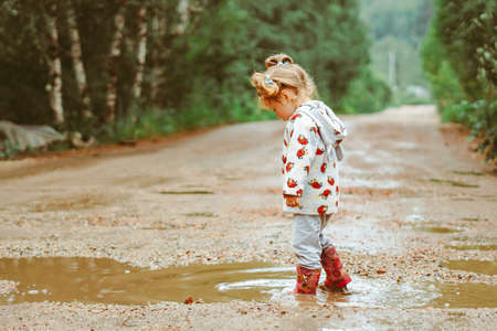 a child runs through puddles in rubber boots