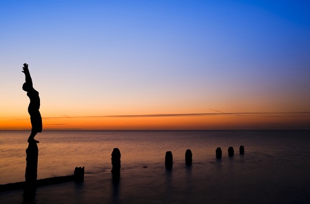 Silhouette of young woman doing exercises on empty beach at sunsetの写真素材