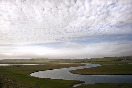Meandering river twists through beautiful countryside landscape with cloudy blue sky overheadの写真素材