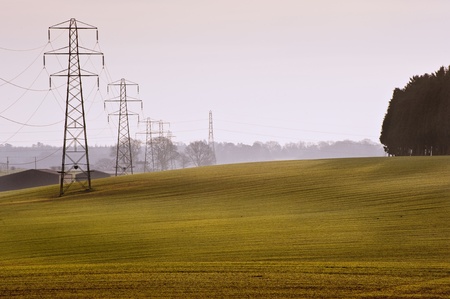 Electricity cable communication towers on sunrise agricultural landscapeの写真素材
