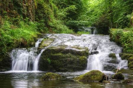 Lush green forest scene with long exposure blurred waterfall flowing through and over rocks covered in lichen and mossの写真素材