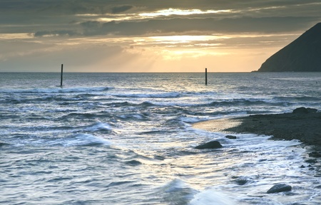 Lovely image of sunrise over incoming tide with rocky foreground and cliffs in backgroundの写真素材