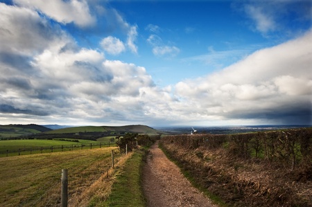 Stunning moody sky with beautiful cloud formations and colors over countryside landscape of path...